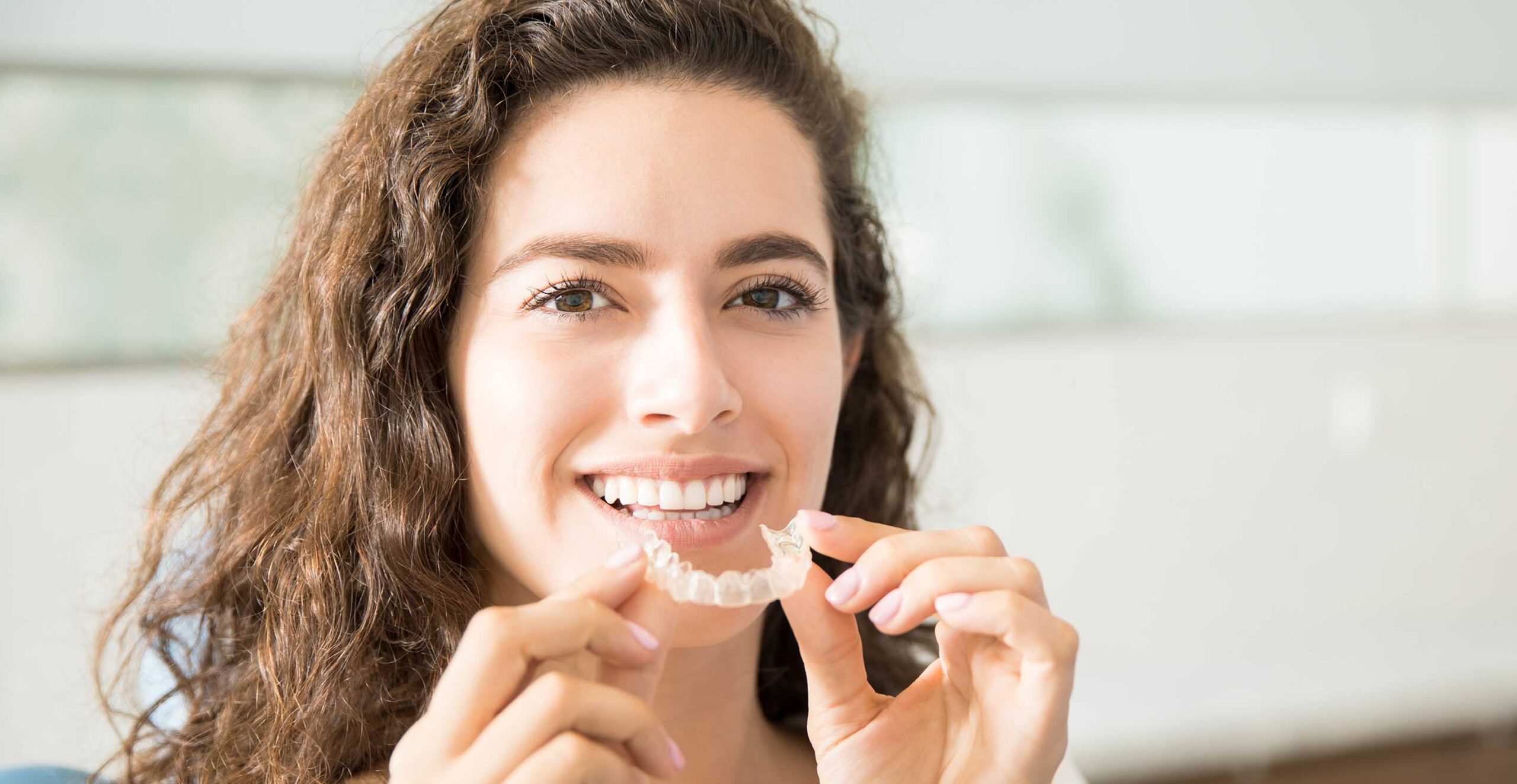 a women smiling whilst holding a pair of clear aligners in her hand